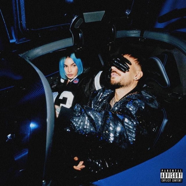 Moody indoor shot of a man with gloved hands over eyes and a woman with blue hair inside a car, bathed in blue light.