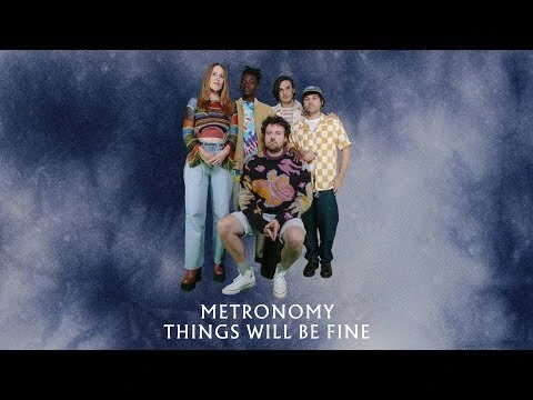 Group of five people posing indoors against a mottled blue backdrop, with visible text 'METRONOMY THINGS WILL BE FINE'.