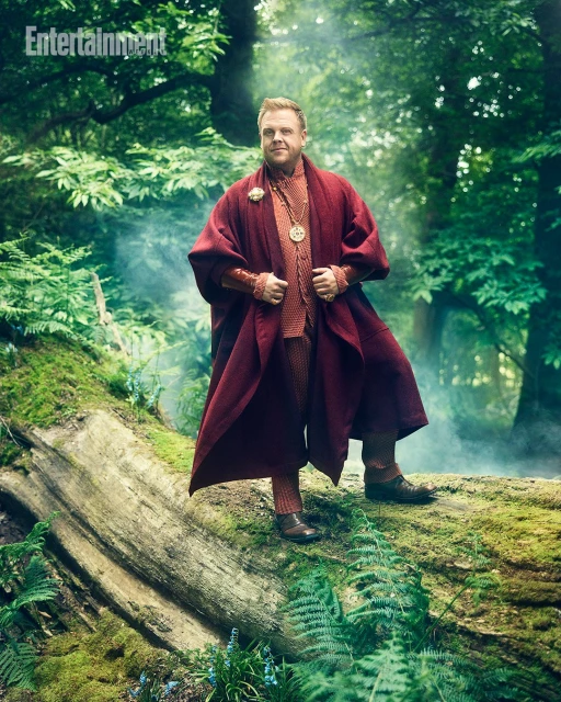 Man in fantasy costume standing on a mossy log in a lush green forest with filtered light and a misty atmosphere, creating a serene scene.