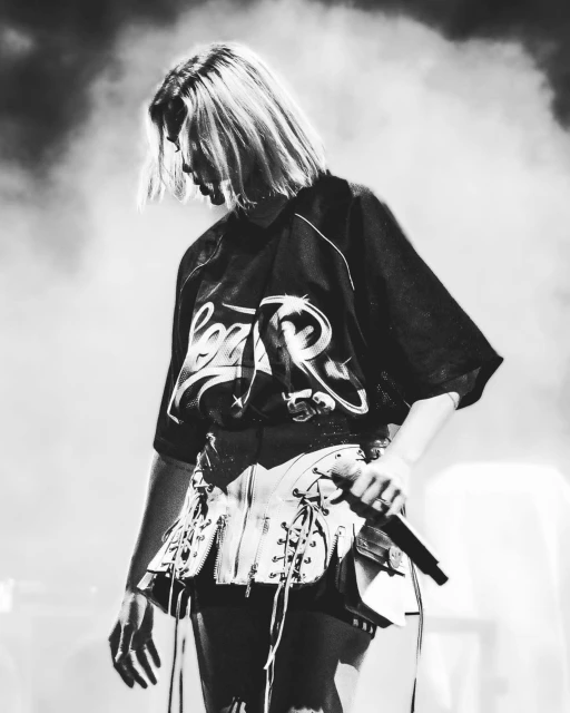 Black and white shot of a singing performer on stage with a microphone and a lace-up leather garment over a dark graphic t-shirt.