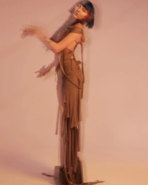 Woman with dark hair poses in a flowing dress in a blurred artistic style against a light pink background, capturing a dreamy aesthetic.