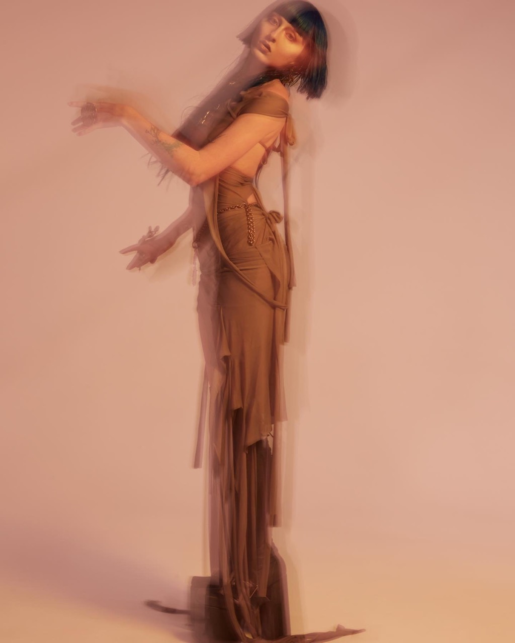 A blurry fashion shot featuring a woman in a green dress, posing in a studio environment with soft lighting, creating an artistic and ethereal feel.