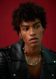 Close-up portrait of a man wearing a black leather jacket and silver chain necklace against a red background.