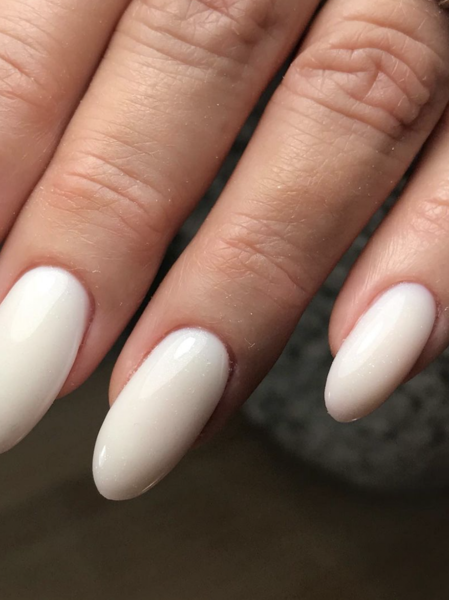 Close-up of an adult human's hand with white manicured fingernails. The nails are almond-shaped, with a clean and polished appearance.