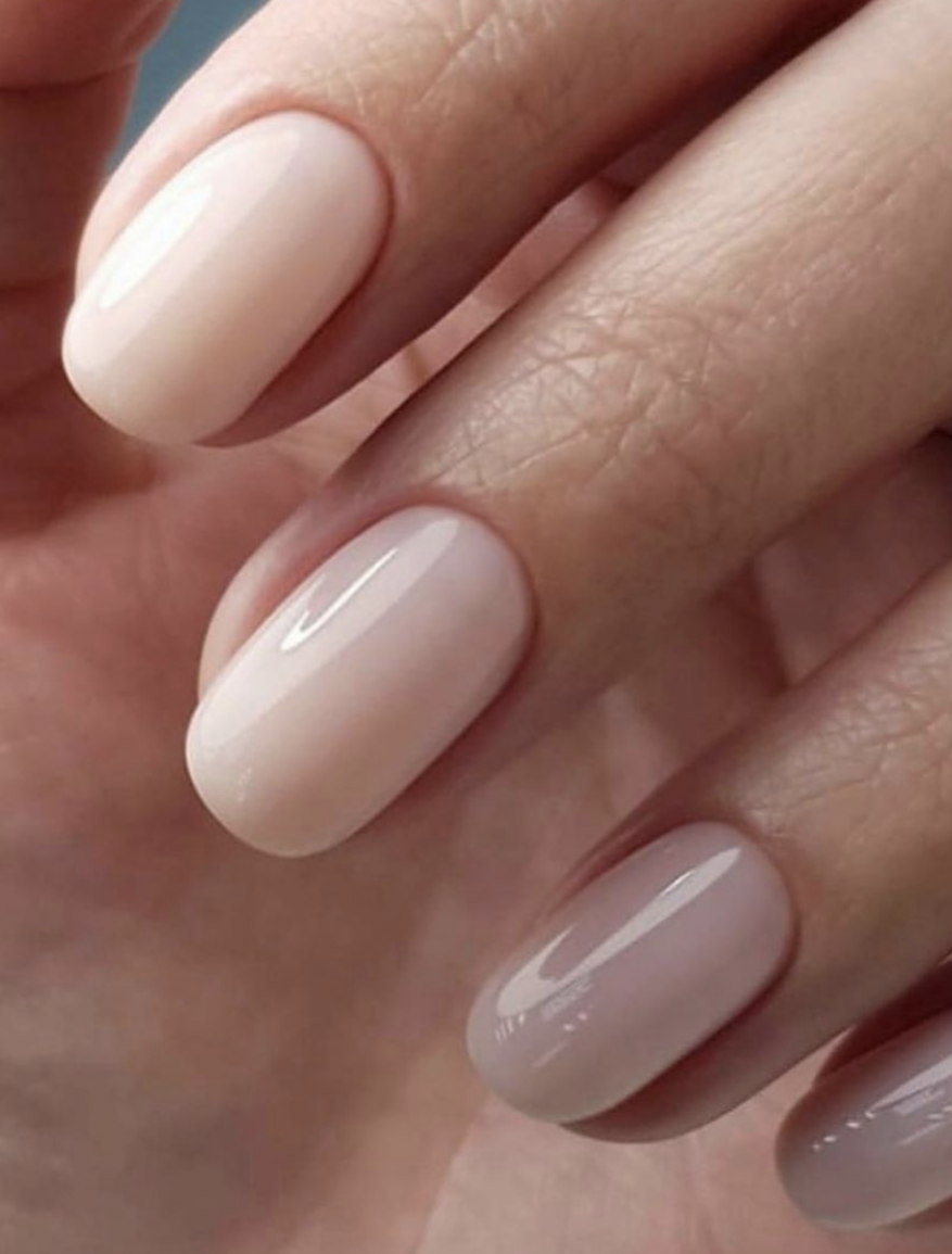 Close-up on a manicured hand showing off oval-shaped nails with glossy, light neutral polish that emphasizes a clean and elegant look.