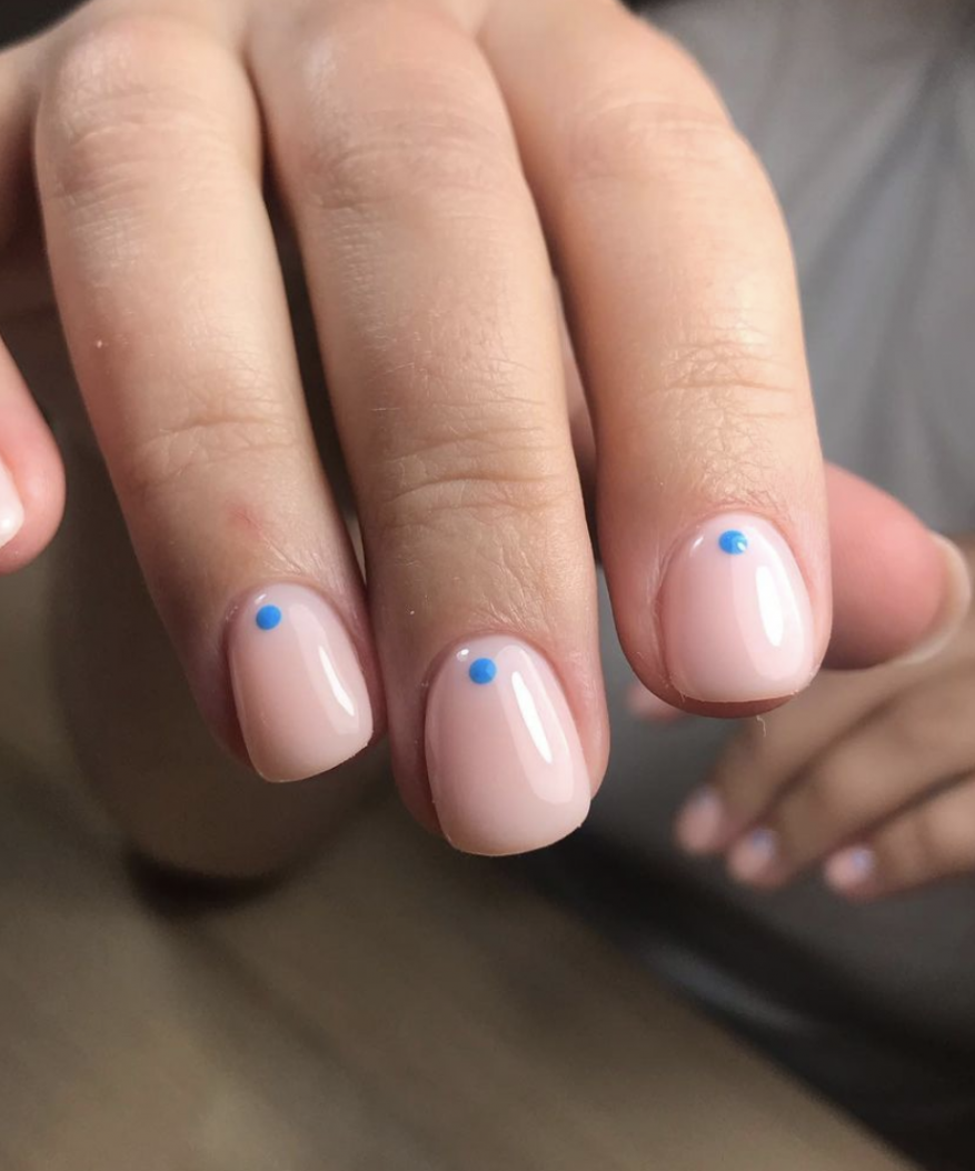 Close-up of manicured nails with short square shape and light pink color with a single turquoise dot on each nail.