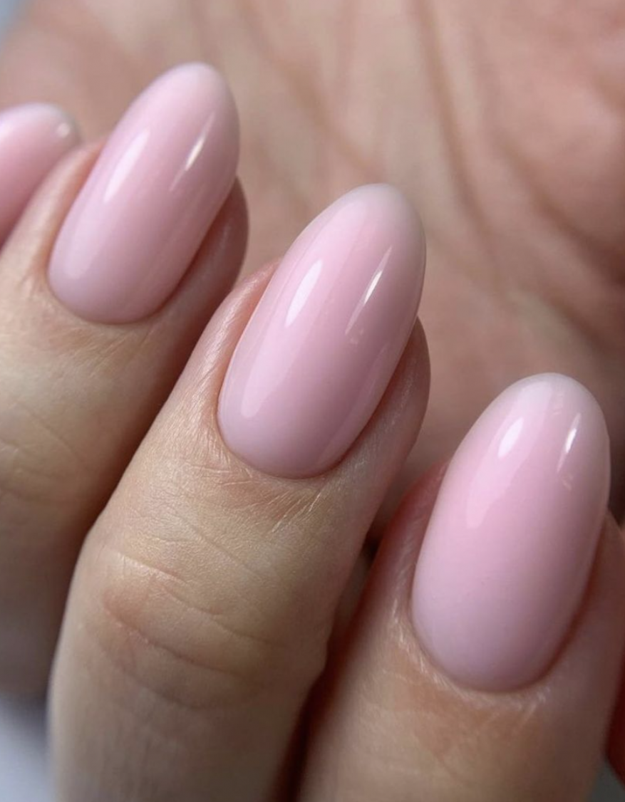 Close-up on a woman's hand displaying pink, rounded acrylic nails, showcasing the beauty and manicure artistry.