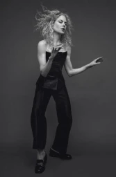 Nicole Kidman with curly blonde hair wearing a dark strapless top and trousers against a grey backdrop