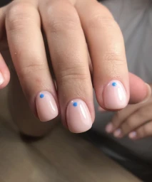 Macro view of short manicured nails with glossy nude polish and a single small blue dot accent at each cuticle by nail artist Cenita Scott