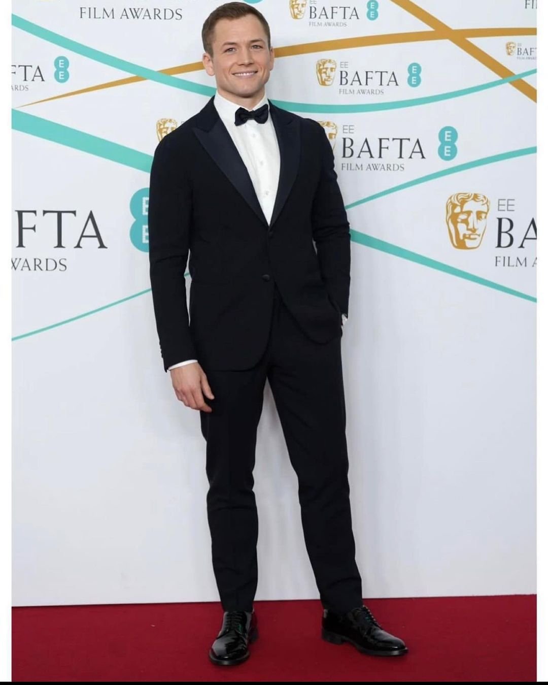 Taron Egerton attends the 75th EE British Academy Film Awards at Royal Albert Hall in black tuxedo and bow tie against a white backdrop.