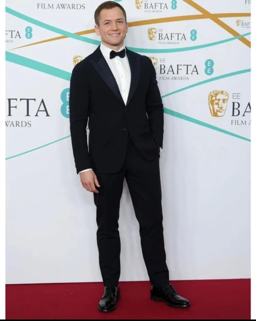 Taron Egerton attends the 75th EE British Academy Film Awards at Royal Albert Hall in black tuxedo and bow tie against a white backdrop.