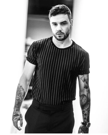 Monochrome portrait of Liam Payne wearing a pinstripe t-shirt and trousers with visible arm tattoos.