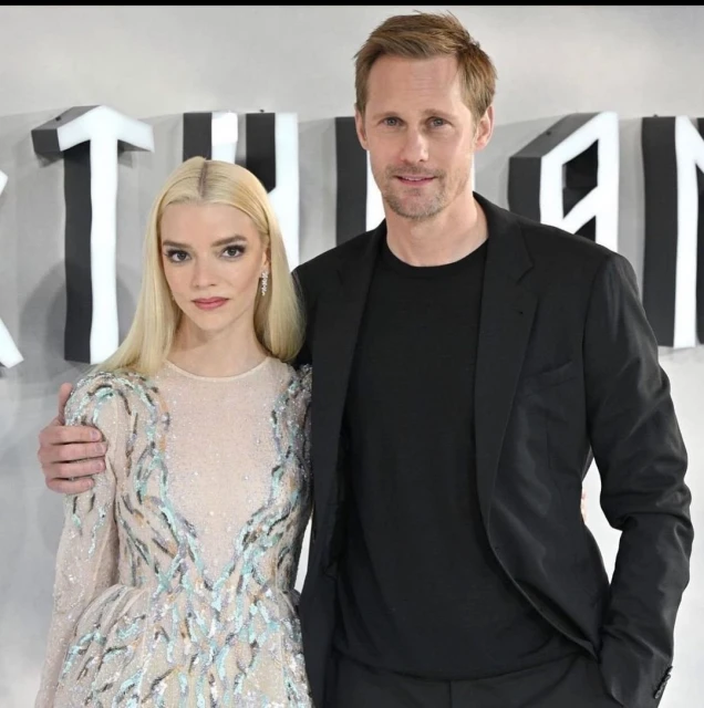 Anya Taylor-Joy and Alexander Skarsgård pose together on a red carpet, with Anya wearing a sequined dress and Alexander in a black suit.