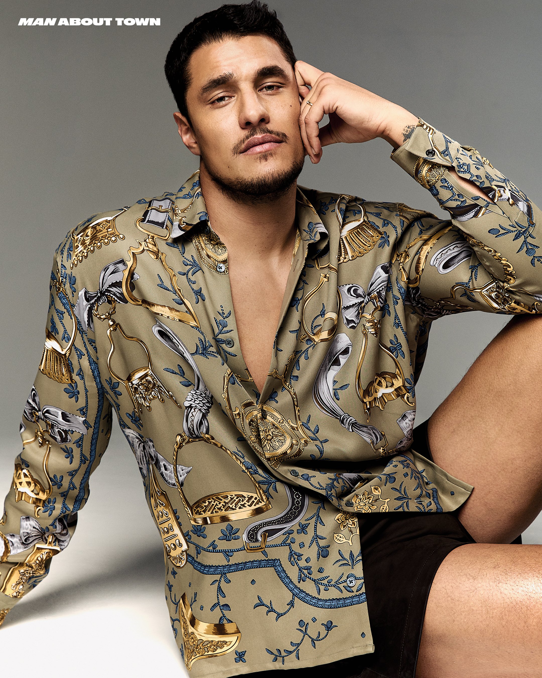 Portrait of a man wearing a patterned button-down shirt, leaning his head on his hand in a studio setting, lit with soft lighting.