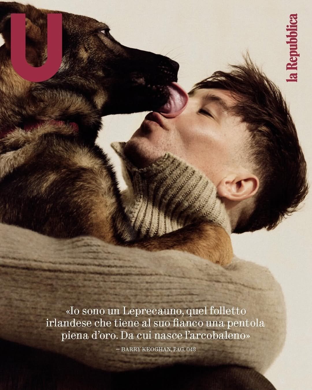 Close-up of a man in a sweater being licked on the face by a brown and black shepherd dog against a plain background.
