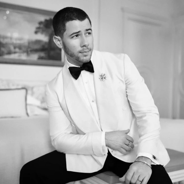 Monochrome portrait of a man in a white suit jacket and black bow tie, seated indoors with soft lighting and a neutral background.