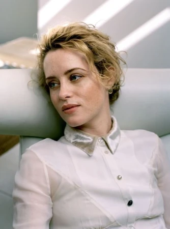 Portrait of a woman with short blonde hair and freckles wearing a white collared shirt, resting against a pale grey headrest in London.