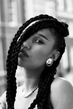 Close-up monochrome portrait of a woman with large braided hair styling, wearing statement earrings and a necklace