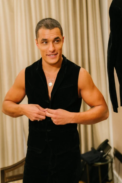 Attractive adult male in black vest buttons garment in indoor setting with soft lighting against neutral background, posing for portrait.
