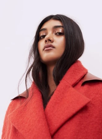 Low angle portrait of a woman wearing a textured bright red coat against a plain white background