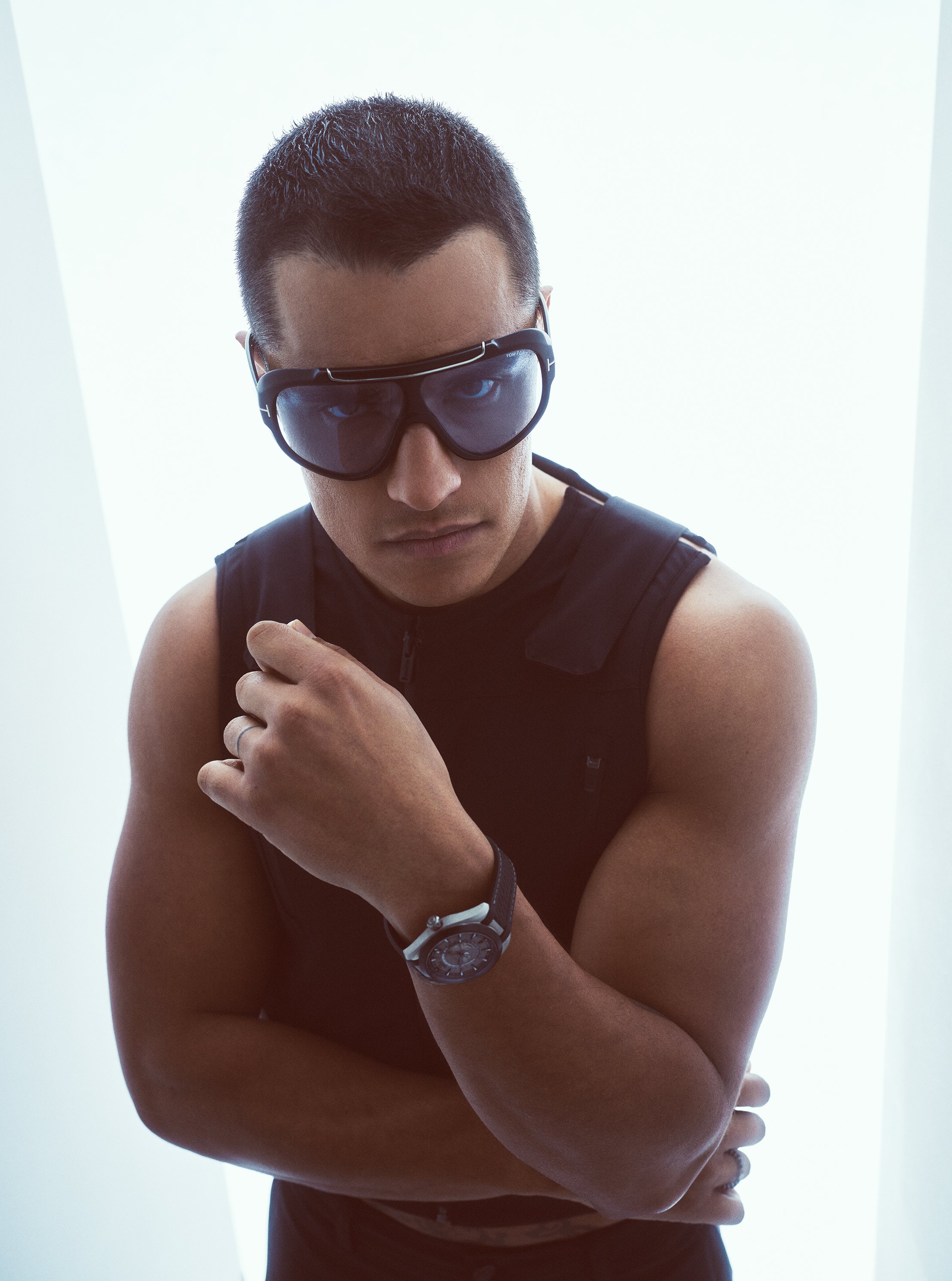 Portrait of an adult male wearing sunglasses and a black sleeveless shirt in a brightly lit studio setting, showcasing a serious facial expression.