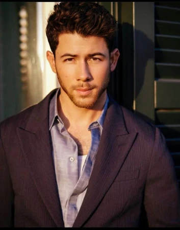 Close-up portrait of Nick Jonas wearing a dark blazer and blue button-down shirt outdoors in natural sunlight.