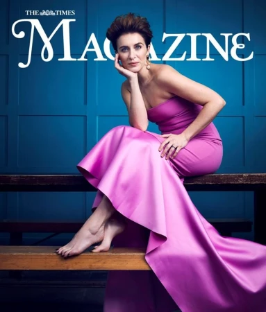Woman in strapless magenta gown seated on a bench against a blue paneled wall for magazine cover portrait