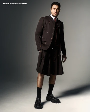 Fashion shot of a man in a dark kilt suit, posing in a photo studio with bright light and gray background for 'Man About Town'.