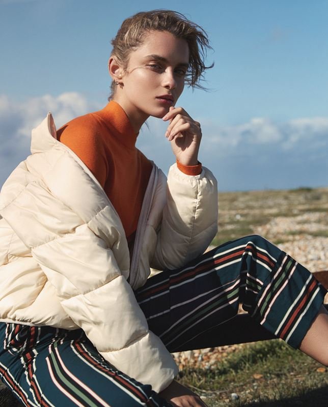 Woman wearing an orange turtleneck and cream puffer jacket outdoors against a clear sky