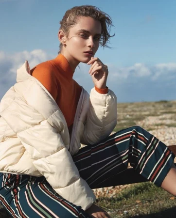 Woman wearing an orange turtleneck and cream puffer jacket outdoors against a clear sky