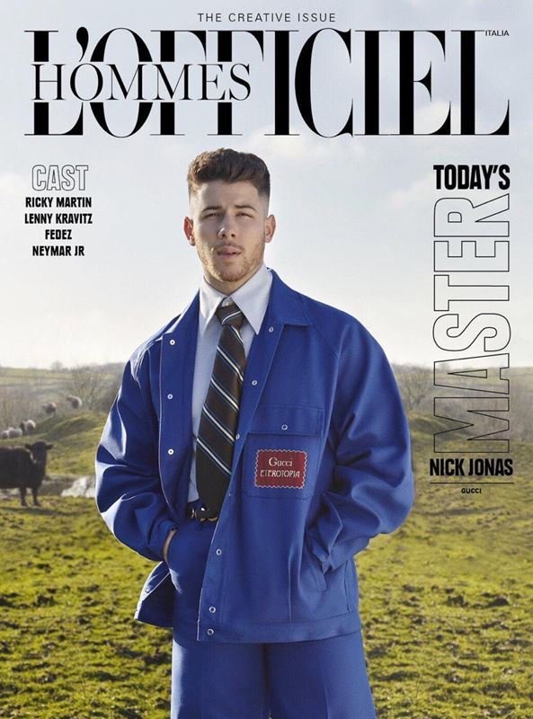 L'Officiel Hommes Italia magazine cover featuring Nick Jonas in a blue jacket, posing outdoors in a field with sheep and cloudy sky.