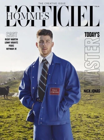 L'Officiel Hommes Italia magazine cover featuring Nick Jonas in a blue jacket, posing outdoors in a field with sheep and cloudy sky.