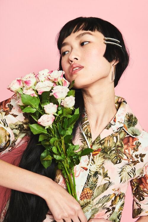 Asian woman in a floral shirt holds a bouquet of pink roses against a pink backdrop, creating a vibrant and eye-catching portrait.