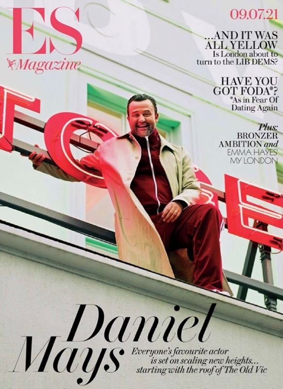 Actor Daniel Mays leaning against a large red neon sign on a rooftop for an ES Magazine cover portrait styled by Charley Mcewen.