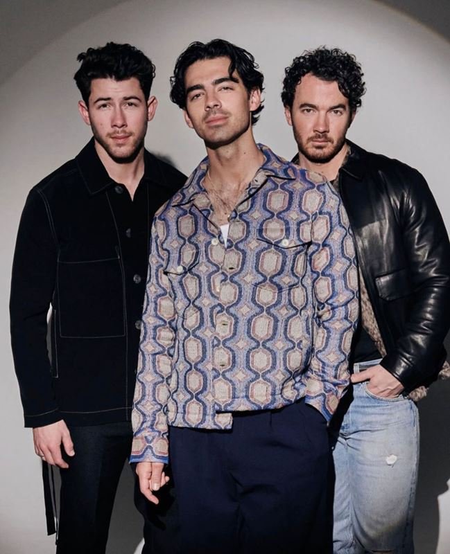 Three men posing together against a plain grey seamless background, styled by hair stylist Charley Mcewen in London.