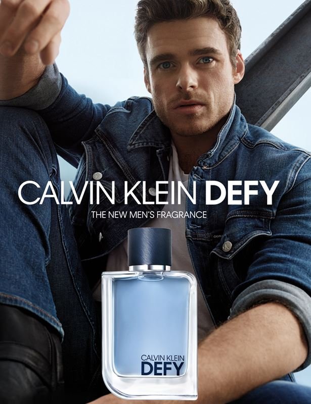 Man in denim jacket poses next to a Calvin Klein fragrance bottle for a product shot, with a blue and white color scheme and logo text.