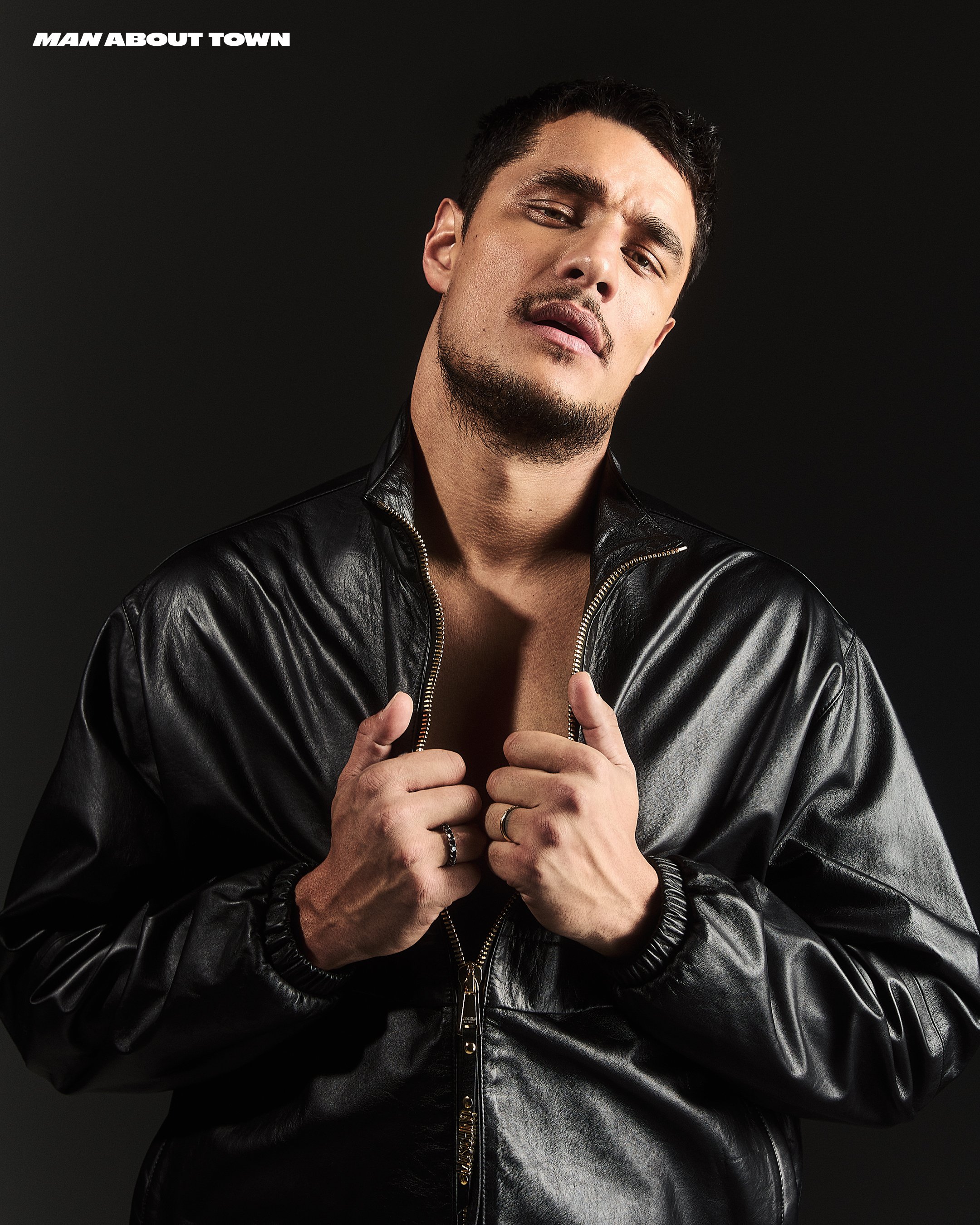 Portrait of a muscular adult male in a black leather jacket against a dark background, showcasing a modern and stylish look with magazine text.