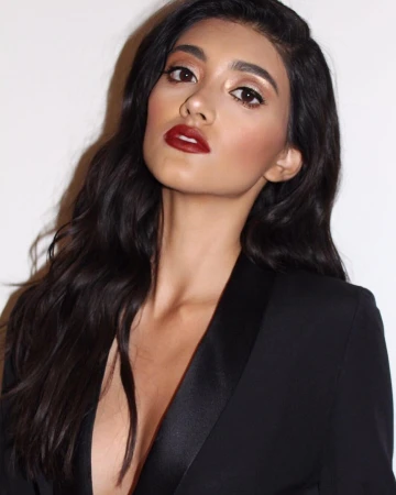 Portrait of a woman with dark wavy hair and red lipstick wearing a black blazer against a plain white background