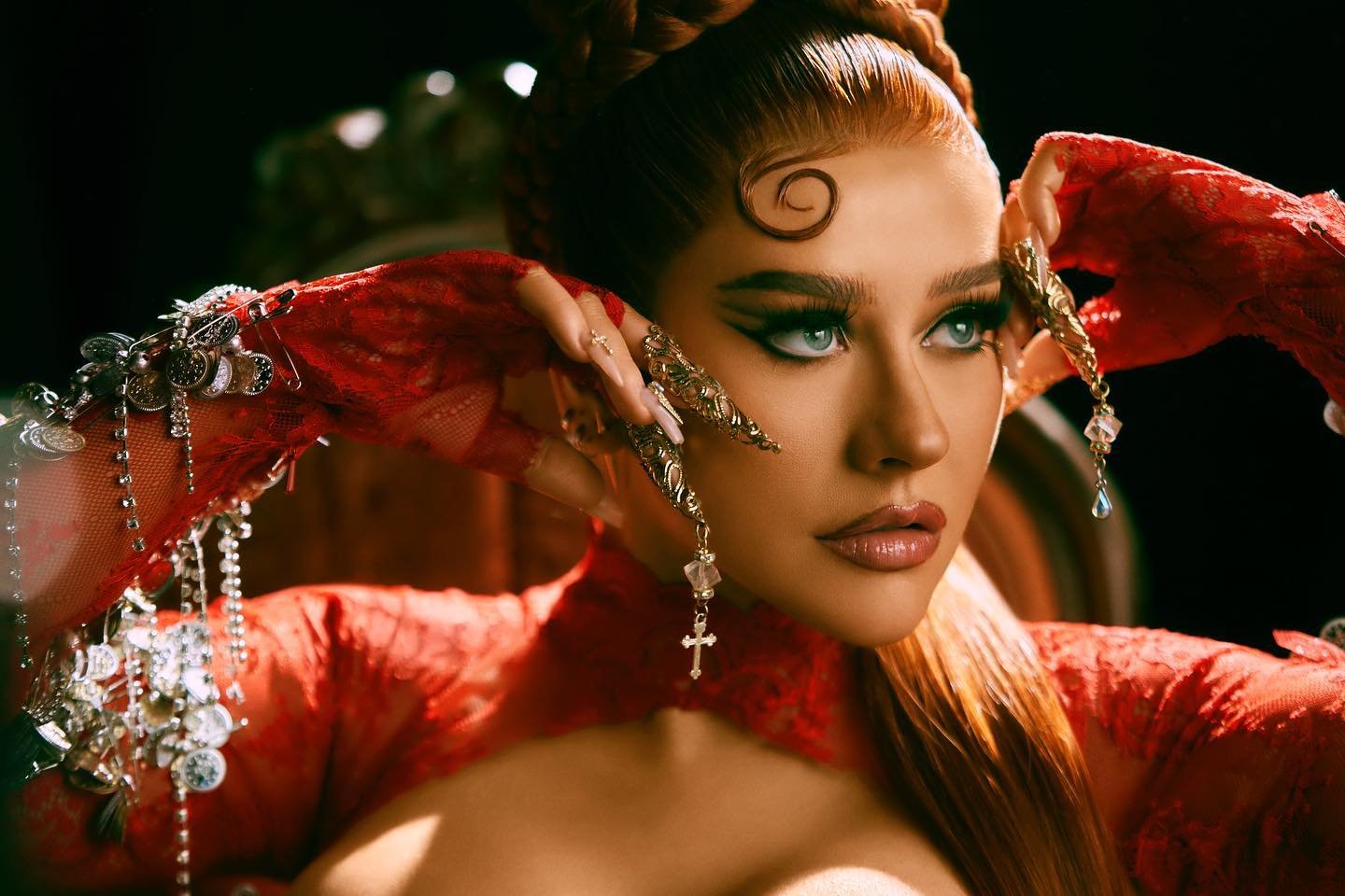 Close-up of Christina Aguilera, an adult female, styled in a red dress with ornate nail jewelry and an elaborate updo hairstyle.