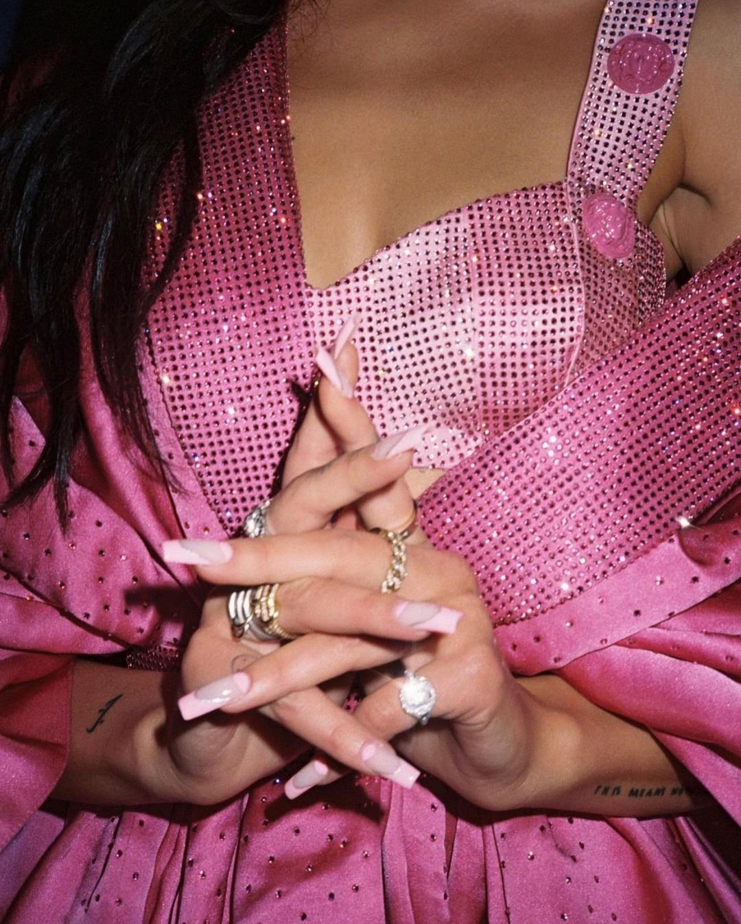 Close-up of a person in pink dress with sparkling details, featuring manicured hands adorned with rings, emphasizing jewelry and fashion.