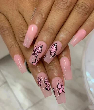 Close-up of a manicured hand with long, square-shaped nails adorned with pink and black butterfly designs on a pale-skinned hand.