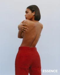 Woman with dark bob haircut wearing red textured trousers against a plain light background