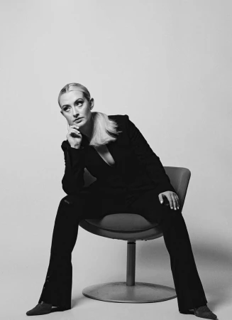 Monochrome portrait of a woman seated in a modern swivel chair wearing a dark pantsuit, styled by Chloe Griffin.