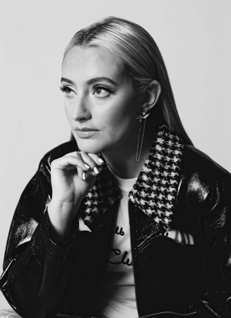 Monochrome portrait of a woman wearing a patterned collar jacket with her hand under her chin.