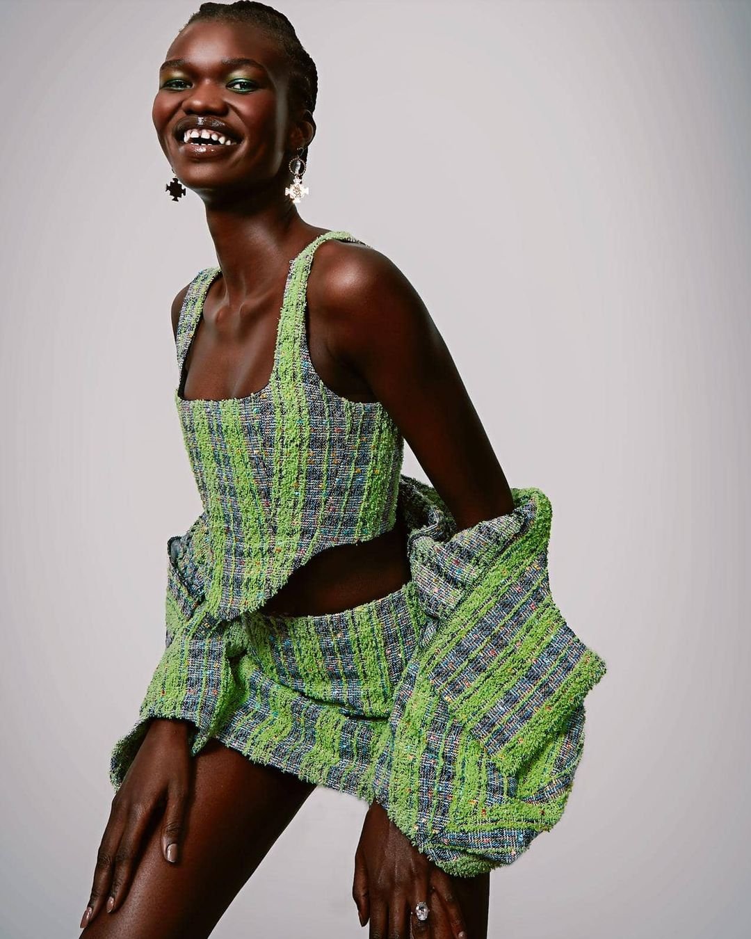 Smiling black model wearing a green tweed crop top and matching skirt styled by Chloe Griffin against a plain white background.