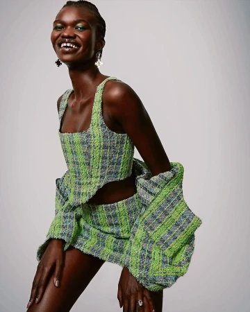 Smiling black model wearing a green tweed crop top and matching skirt styled by Chloe Griffin against a plain white background.