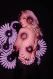 Portrait of a blonde woman with floral pattern light projections cast across her back and shoulders
