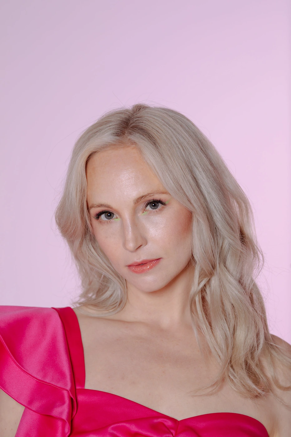 Portrait of a blonde woman wearing a vibrant pink satin top against a soft pink seamless background.