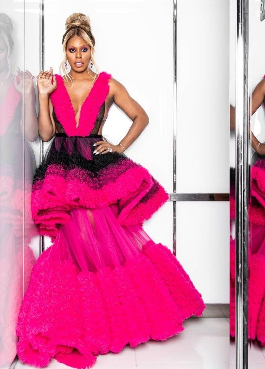 Elegant adult woman with blonde hair in a hot pink and black gown posing indoors with a confident expression and jewelry.