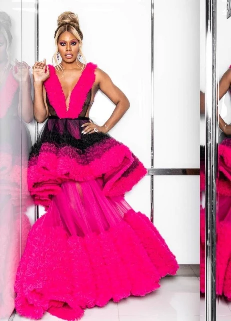 Elegant adult woman with blonde hair in a hot pink and black gown posing indoors with a confident expression and jewelry.